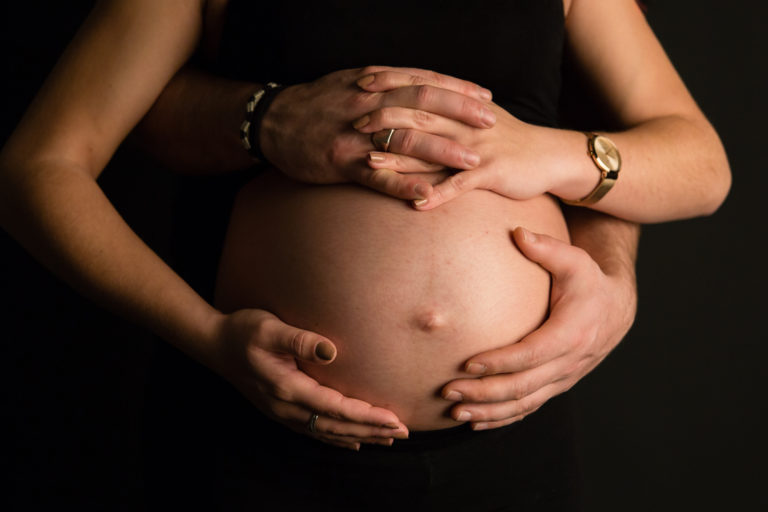Ventre de femme enceinte, photo de grossesse sur fond noir avec des mains posées - Oise -