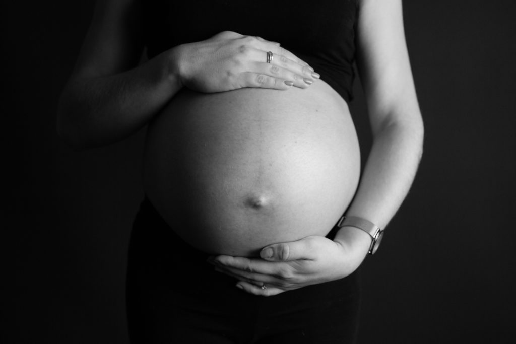 Ventre de femme enceinte, photo de grossesse sur fond noir avec des mains - Oise -