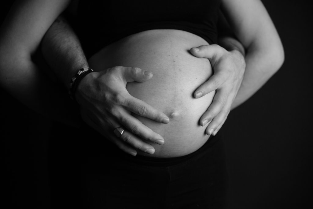 Ventre de femme enceinte, photo de grossesse sur fond noir avec des mains - Oise -