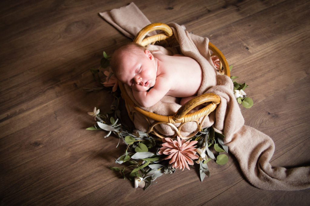 Séance photo nouveau né fille en studio dans l’Oise positionnée dans un panier entourée de fleur