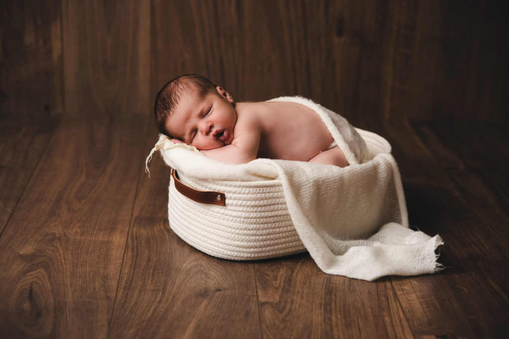 Séance photo nouveau-né garçon en studio dans l’Oise positionnée dans un panier beige