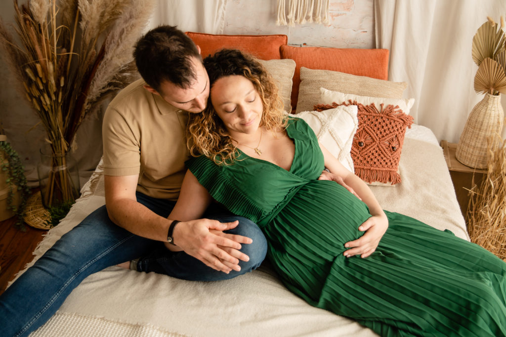 Séance photo grossesse en studio couple femme enceinte sur un lit décor bohème avec une robe verte