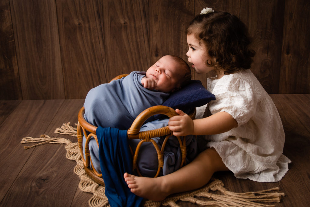 Séance photo nouveau né garçon et de sa soeur en studio dans l’Oise positionnée dans un panier couleur bleu
