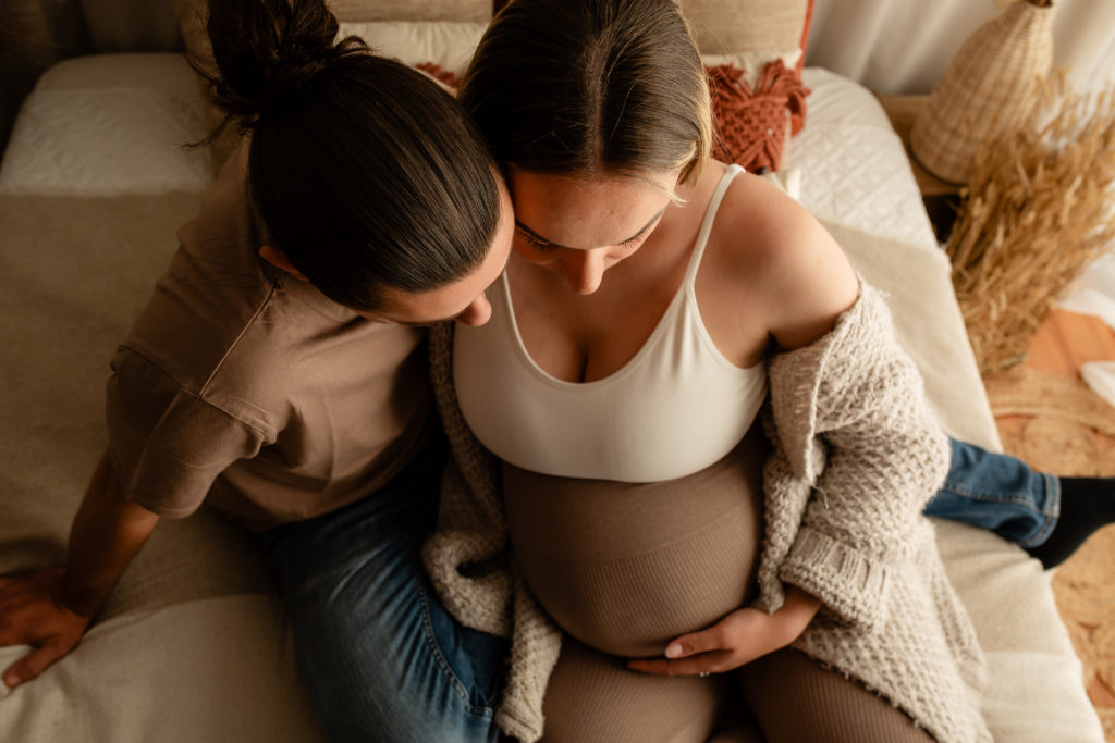 Séance photo grossesse en studio couple femme enceinte sur un lit décor bohème