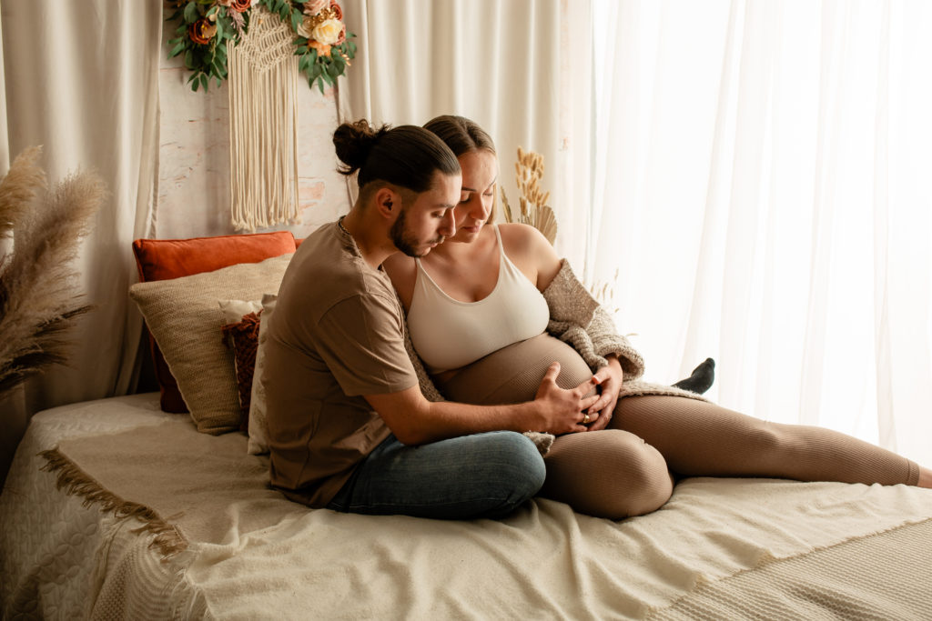 Séance photo grossesse en studio couple femme enceinte sur un lit décor bohème