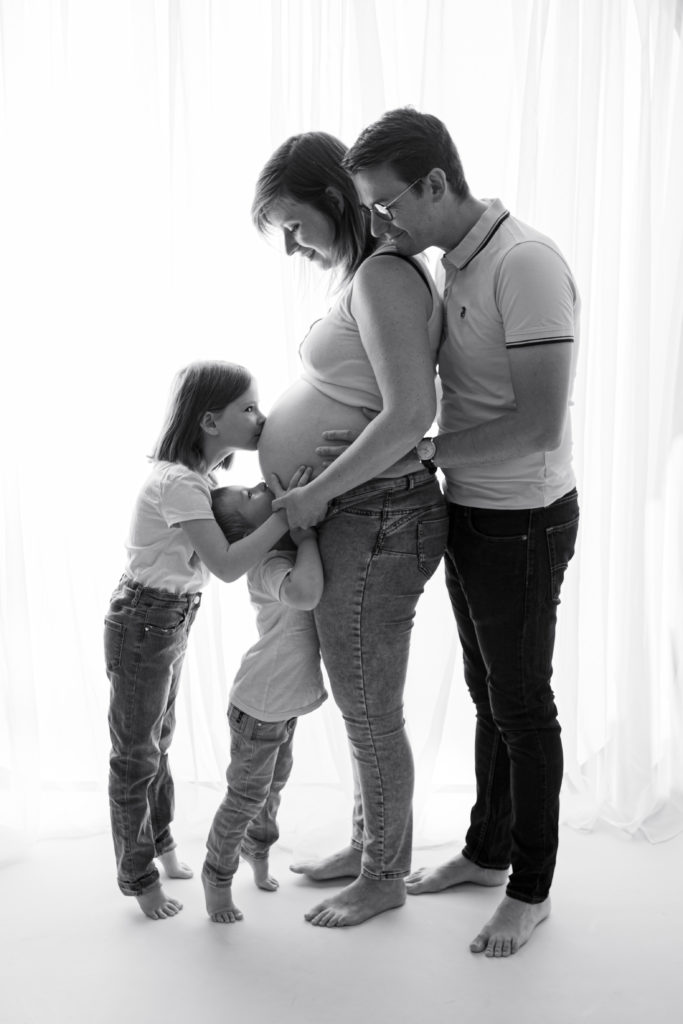 Séance photo grossesse en studio femme enceinte devant une fenêtre en noir et blanc et en famille