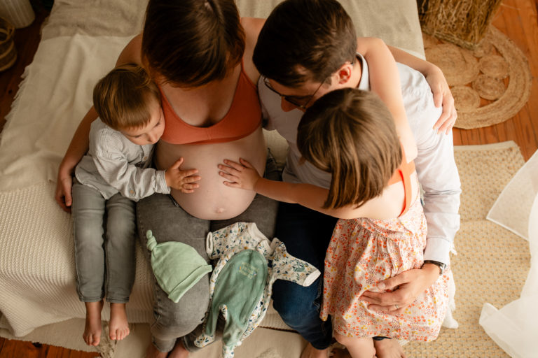 Séance photo grossesse en studio en famille sur un lit décor bohème avec vêtement de bébé