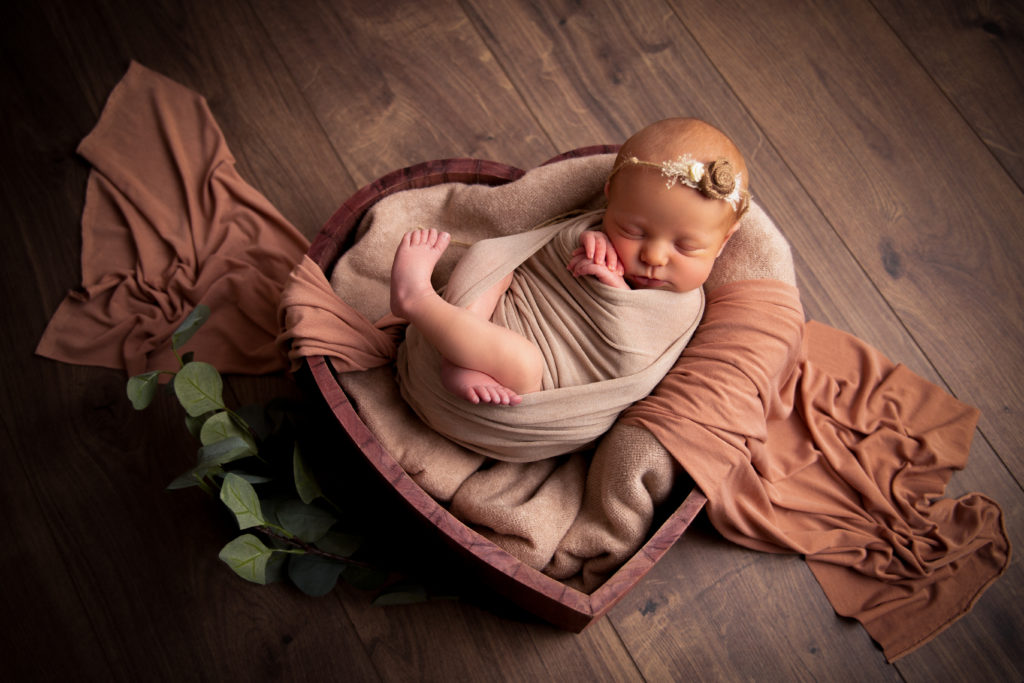 Séance photo en studio de nouveau-né dans l’Oise posé dans un coeur en bois