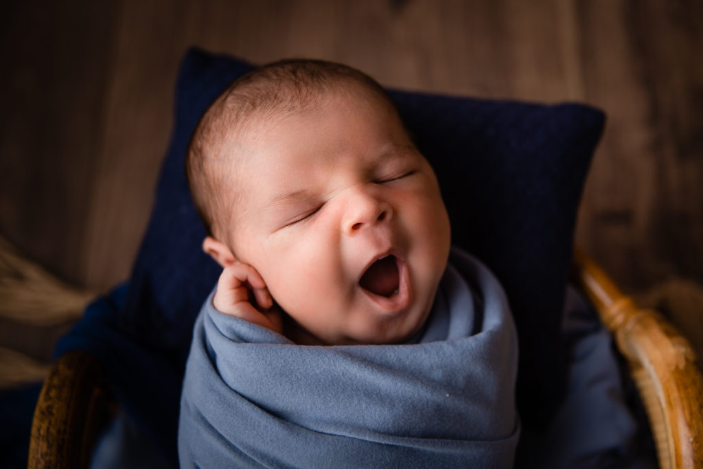 Séance photo nouveau né garçon en studio dans l’Oise positionnée dans un panier couleur bleu en train de bailler