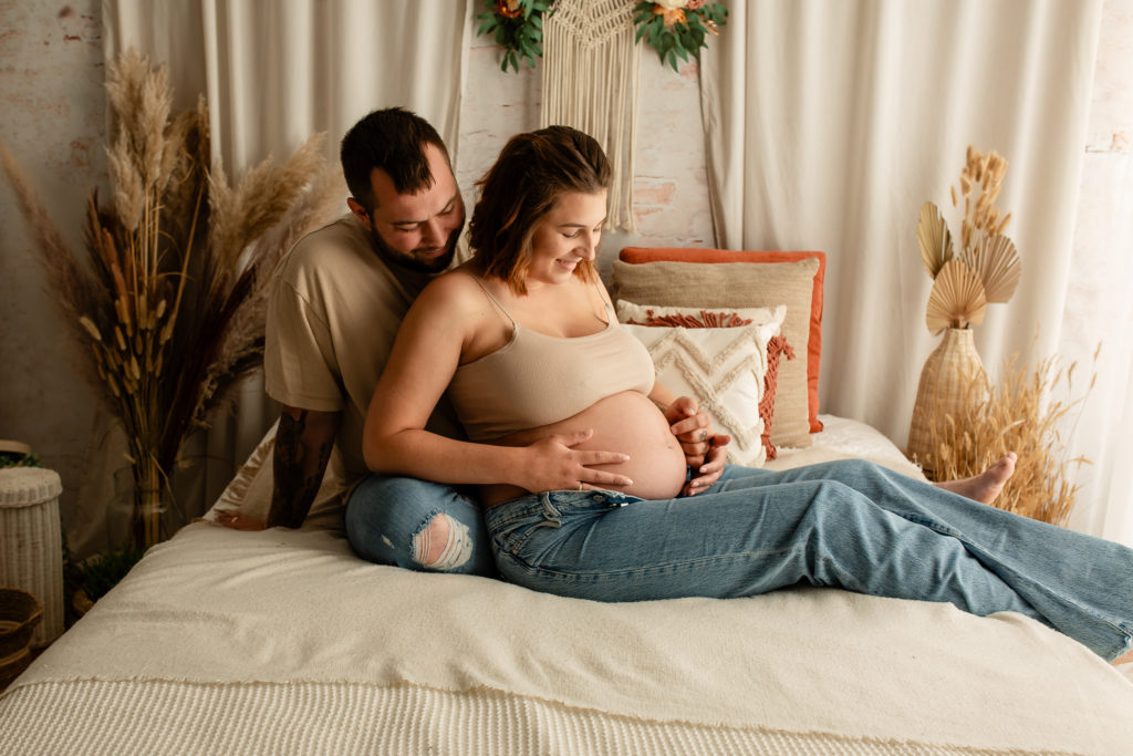 Séance photo grossesse en studio couple femme enceinte sur un lit décor bohème
