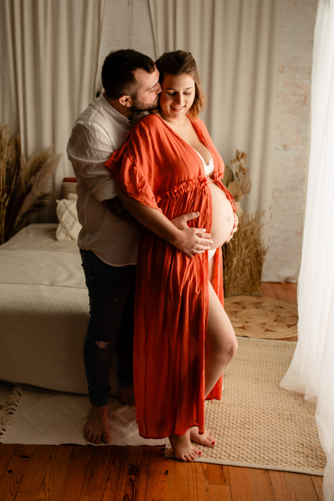 Séance photo grossesse en studio couple femme enceinte sur un lit décor bohème